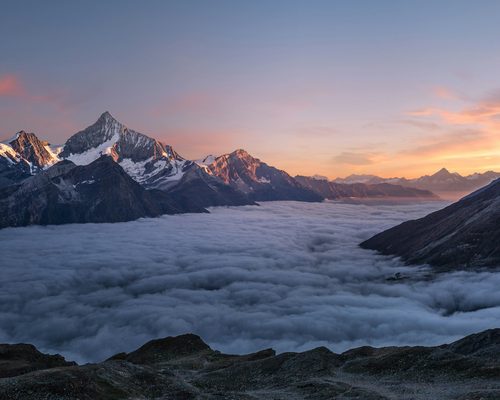 Alpine Lake at First Light: snow peaks above a sea of clouds at dawn