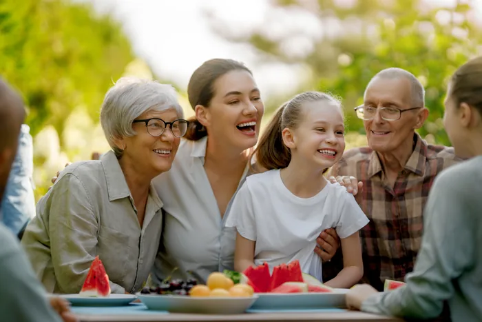 Summer Fruit Picnic: three generations laughing around a table of watermelon and fruit outdoors