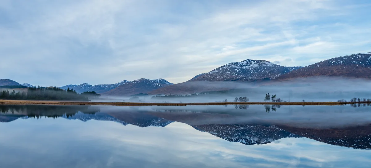 Winter Reflections: snowy hills and low mist mirrored in a still lake